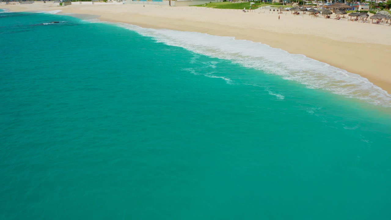 Aerial view over turquoise ocean and a diagonal line of white waves on sand in Baja California Sur, with no visible people.