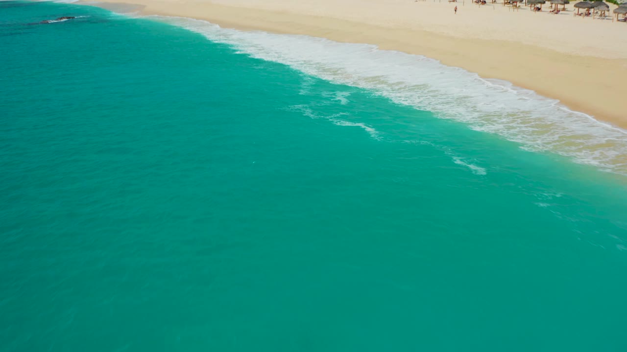 Wide overhead frame of blue-green ocean, white surf, and pale beach in Baja California Sur, with no visible people discernible.