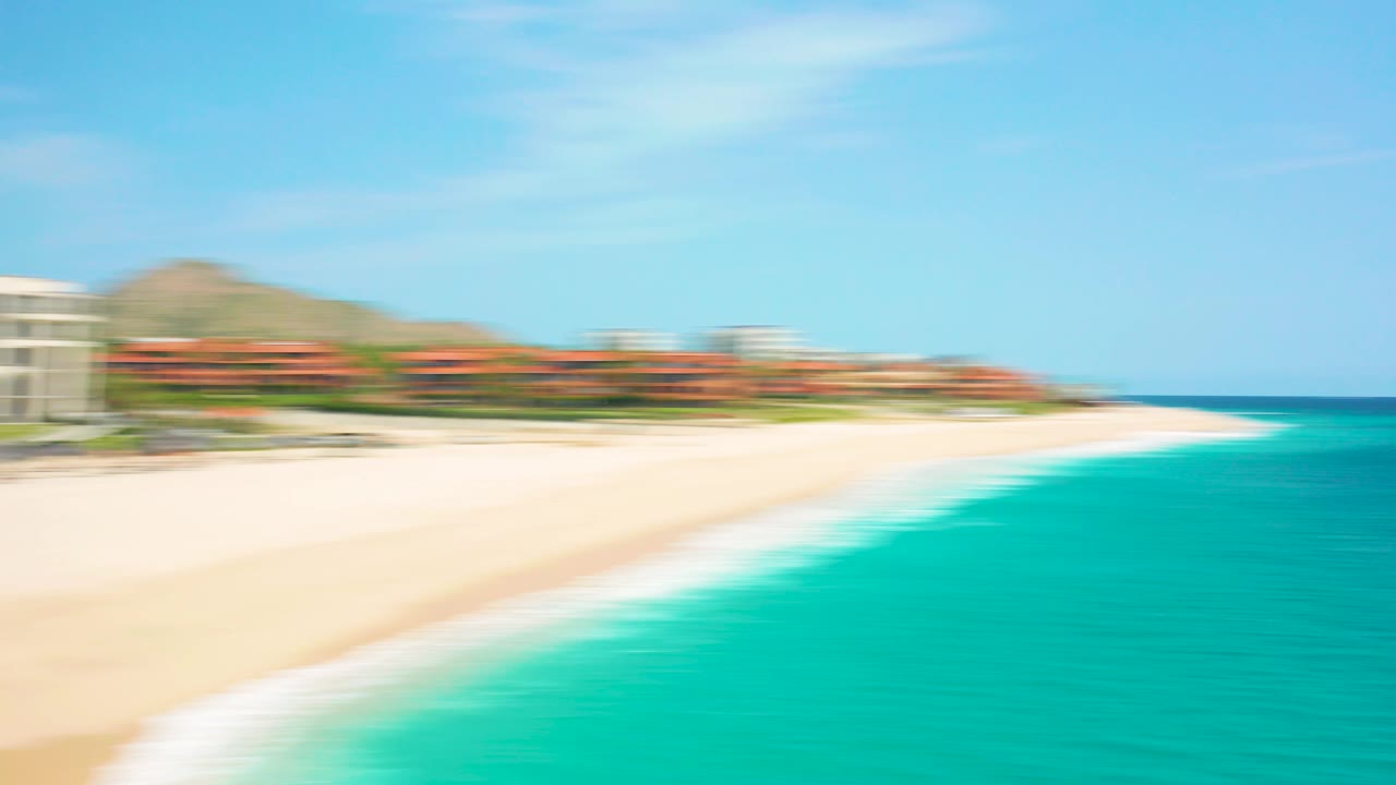 A wide aerial view at Desert Park Natural Reserve in Baja California Sur shows the beach sweeping toward open turquoise water, resort buildings on the left, and no visible people.