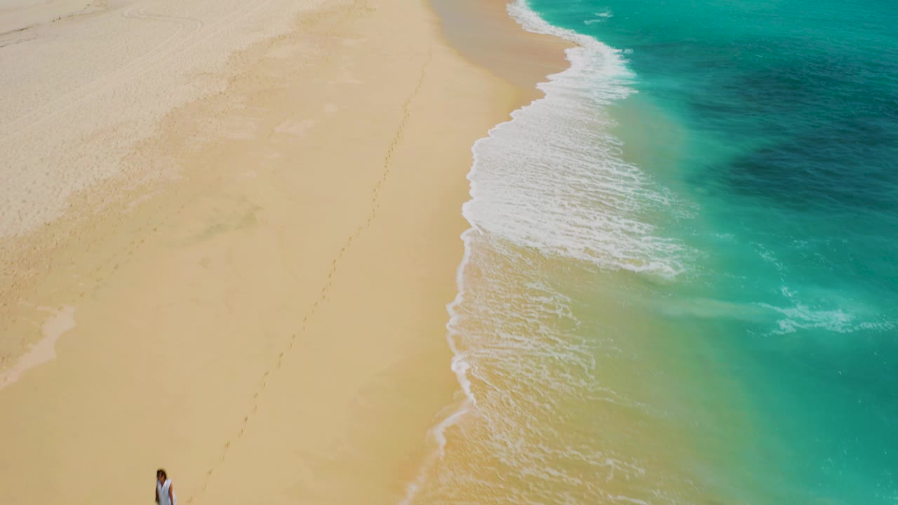 High-angle aerial frame over Desert Park Natural Reserve beach in Baja California Sur, with turquoise water curling onto pale sand and no clearly identifiable people.