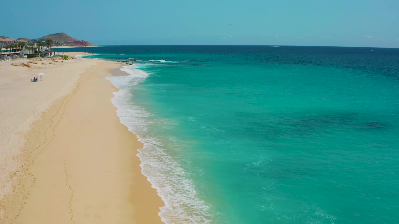 Turquoise surf curves along a wide sandy shoreline