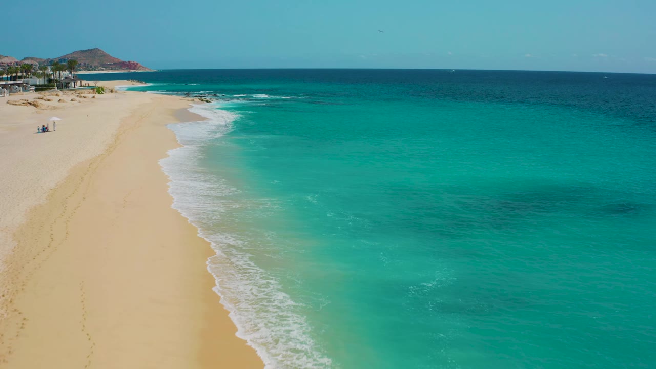 Drone-style view over Desert Park Natural Reserve coastline with the beach on the left, bright turquoise sea on the right, white wash at the edge, and no visible people.