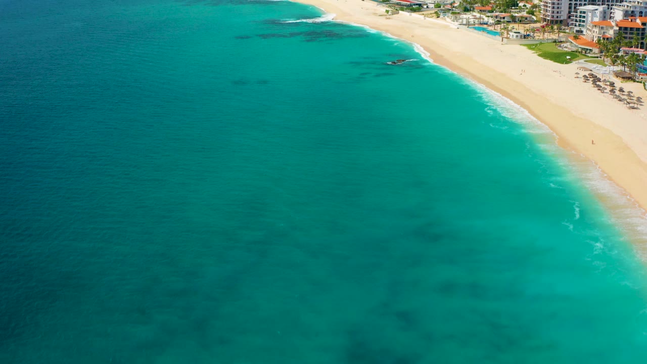 High aerial view over Desert Park Natural Reserve in Baja California Sur, Mexico, with turquoise water, pale beach, dark submerged patches, and no visible people.