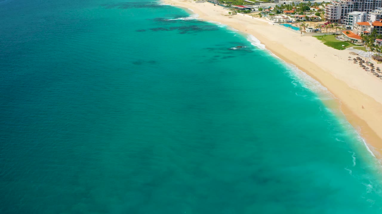 Aerial coastline view with turquoise sea, sandy beach, and dark underwater patches.