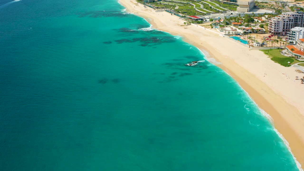 Aerial coastline view with aquamarine water, pale sand, and hotels along the beach.