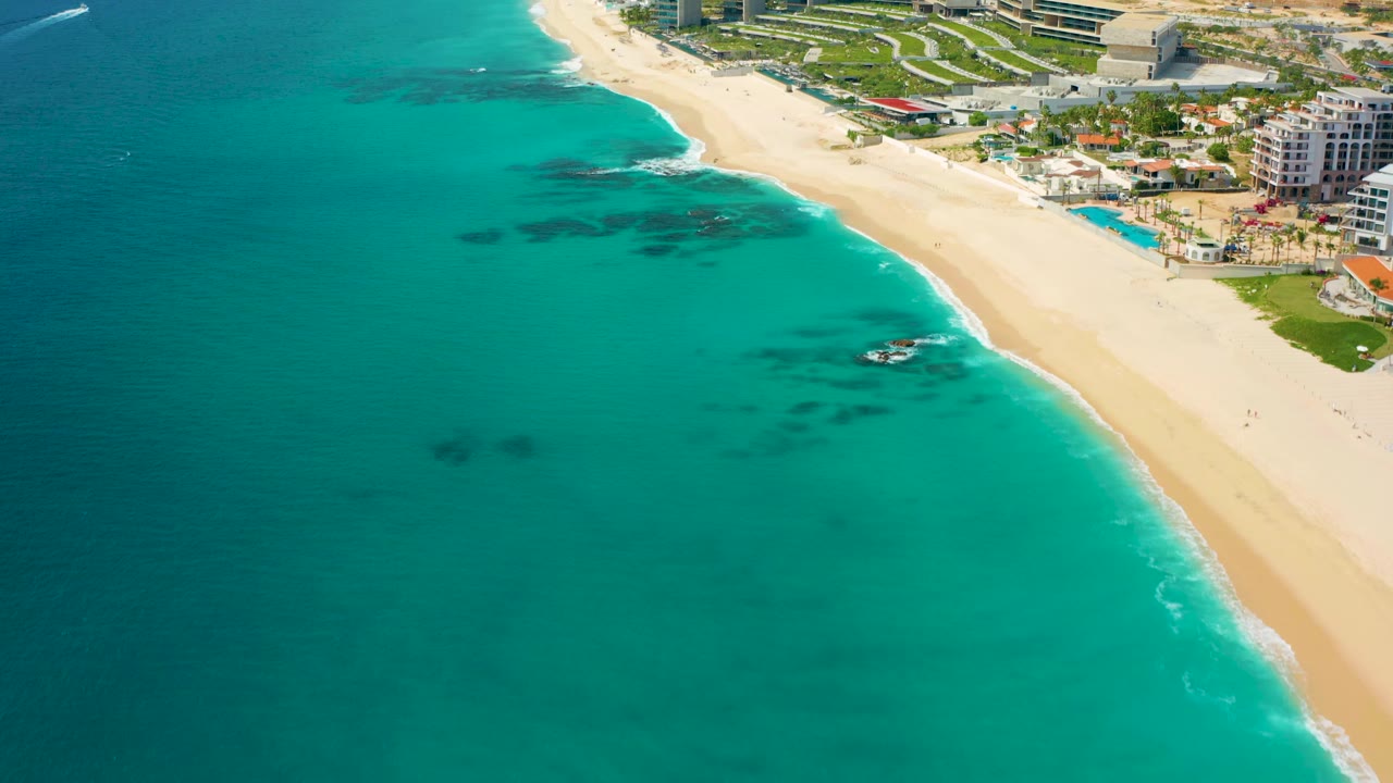 Aerial view of clear blue-green ocean, sandy beach, and resort strip.