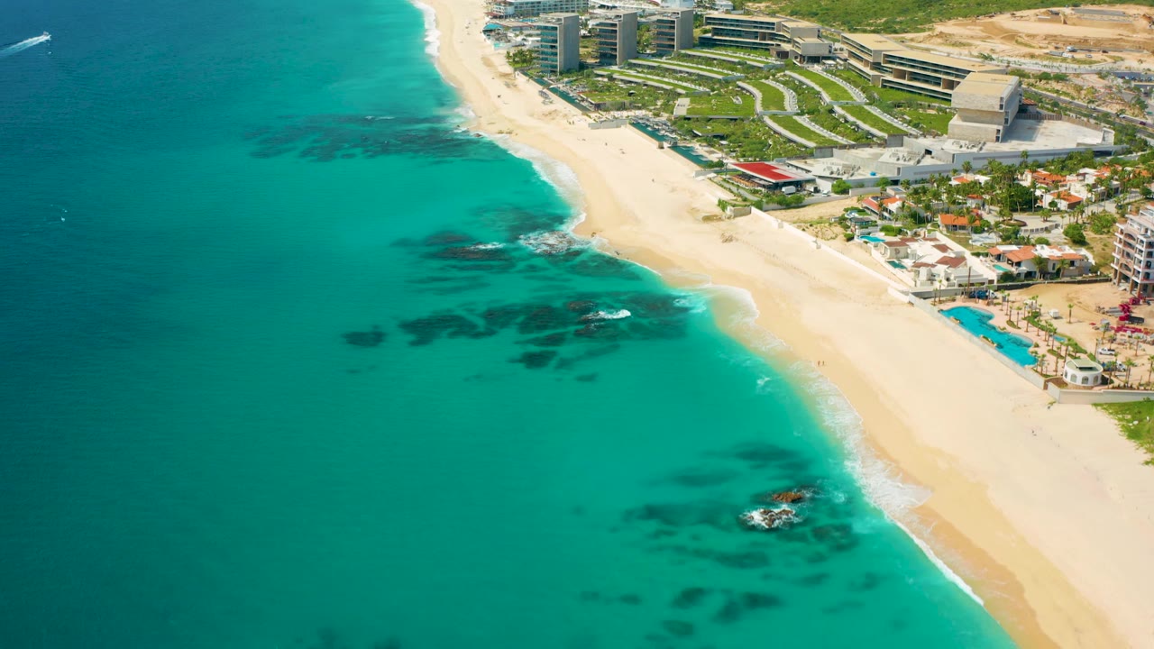 Drone view of beach, turquoise ocean, and resort edge