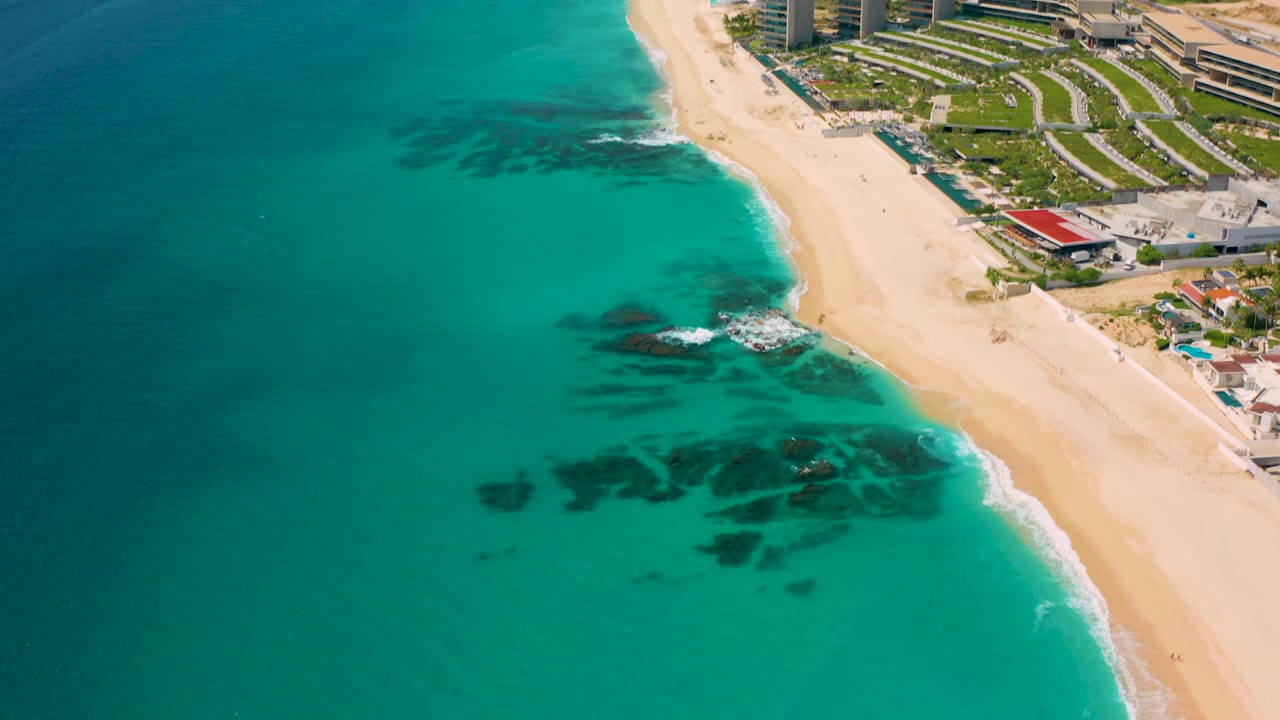 Aerial shoreline with turquoise sea, sandy beach, and resort-style development.