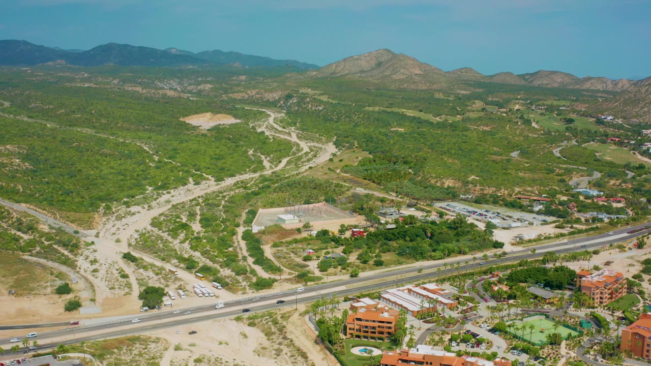 Wide aerial landscape with highway traffic, desert vegetation, and distant mountains.