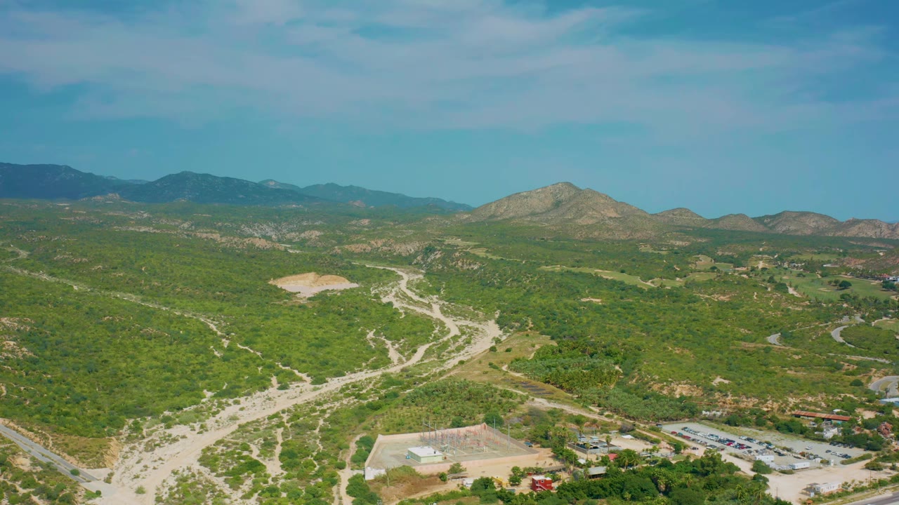 Aerial view in Desert Park Natural Reserve with branching dirt roads across scrub-covered hills, a low mountain horizon, scattered clouds, and no visible people.