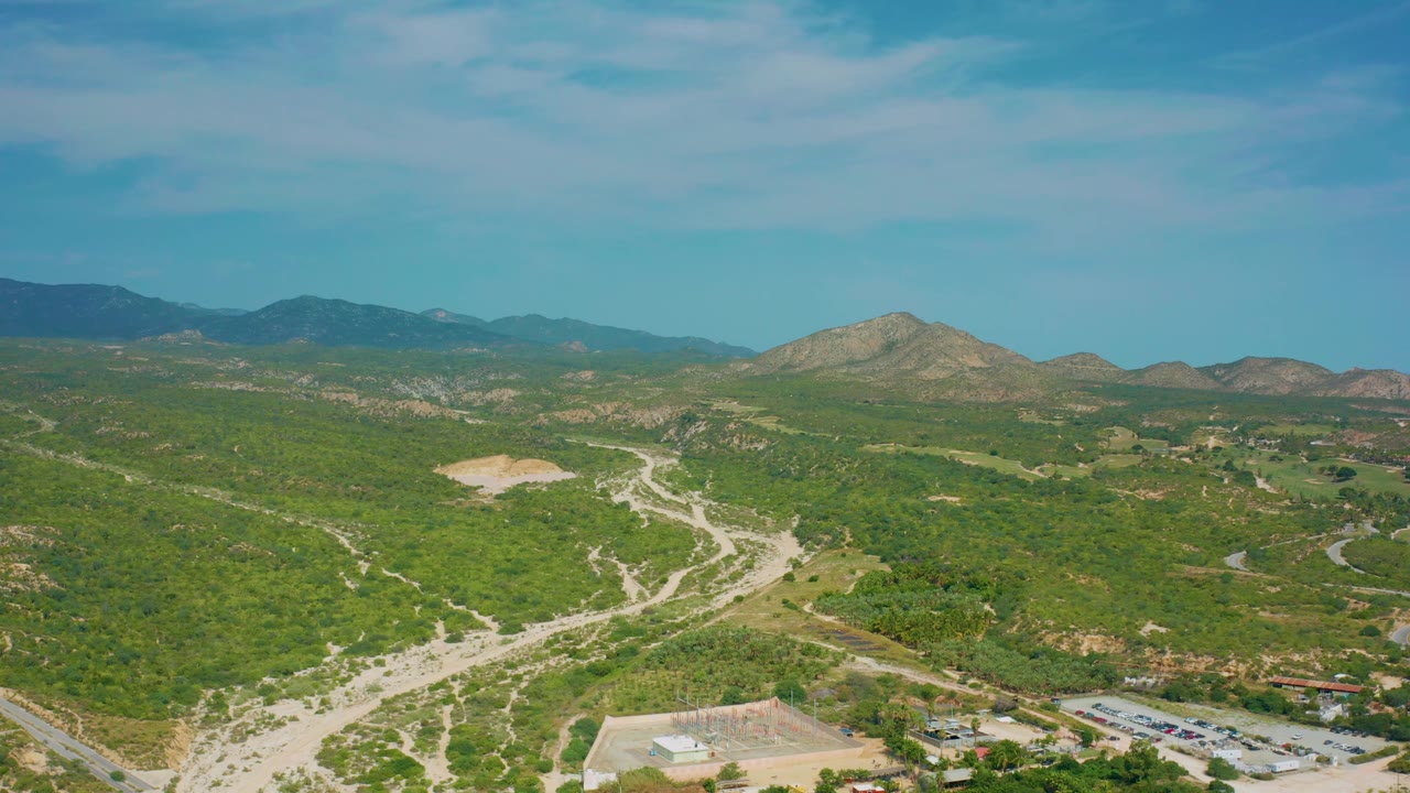 Mid-clip aerial view of Desert Park Natural Reserve showing dusty tracks across green slopes, distant ridgelines under a blue sky, and no visible people.