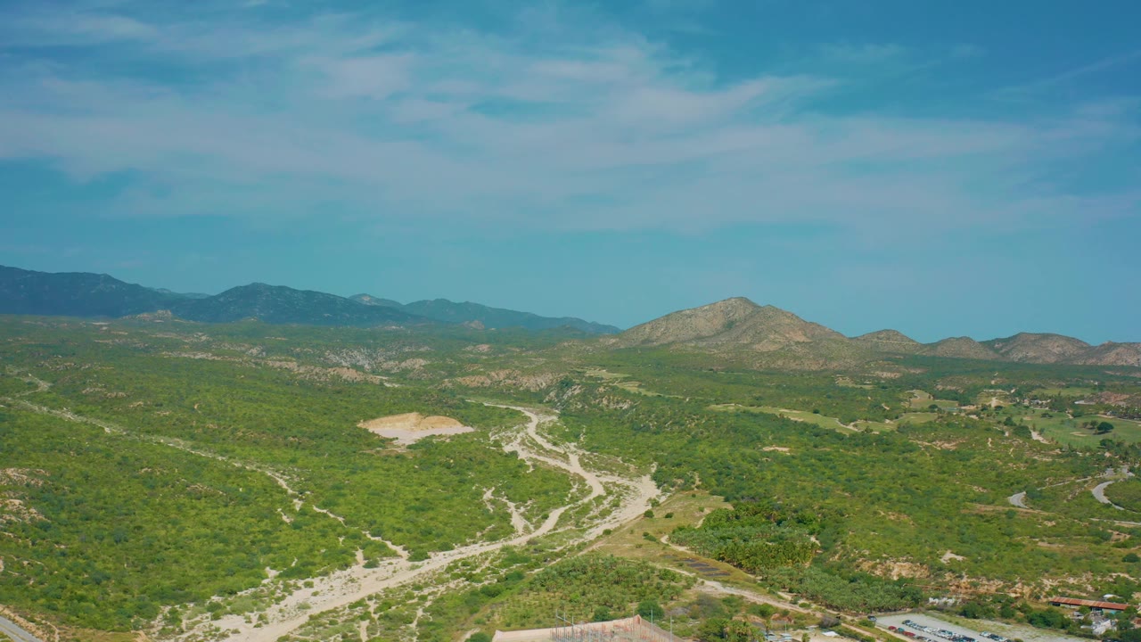 Three seconds in, the reserve view shows pale wash lines and road cuts through green scrub, with a low mountain range in the background and no visible people.