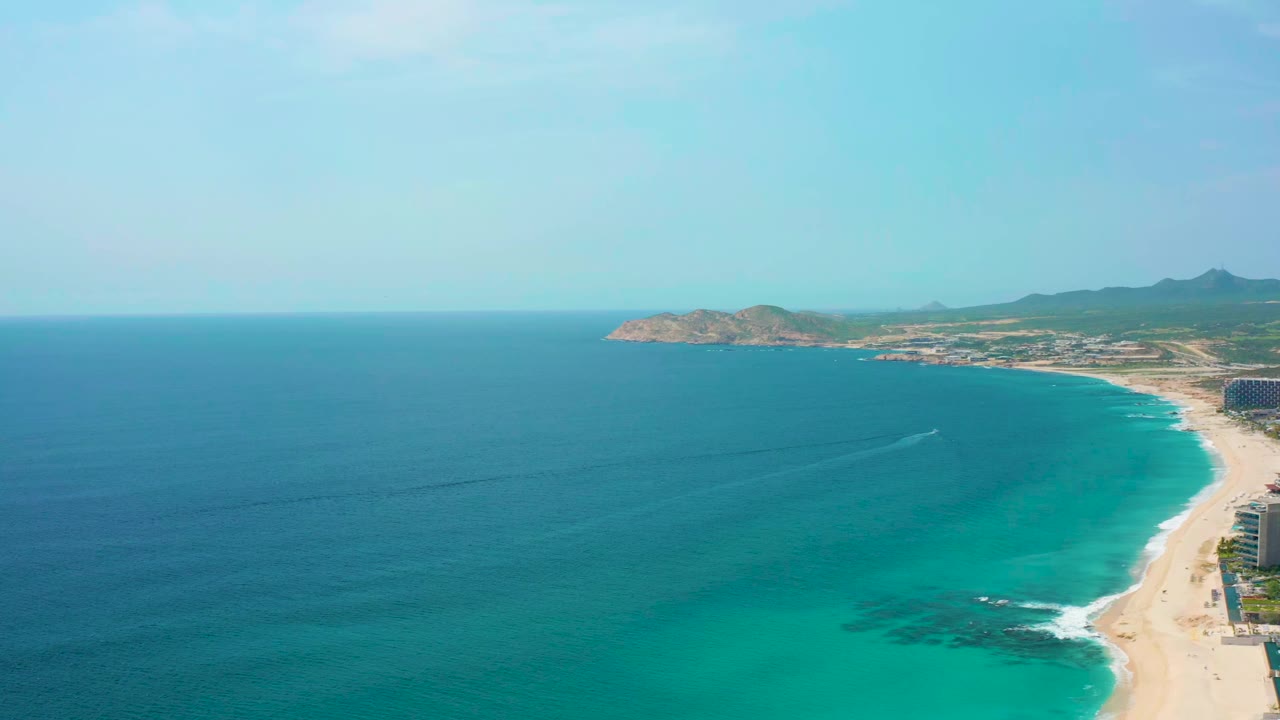 Wide aerial view of turquoise ocean curving along a sandy beach.