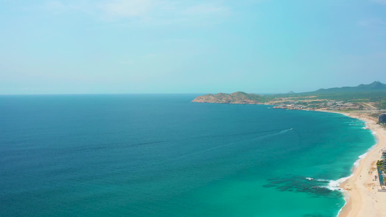 Aerial view of Desert Park Natural Reserve with a broad blue ocean foreground, curved sandy shore to the right, rocky headland, low hills, and no visible people.