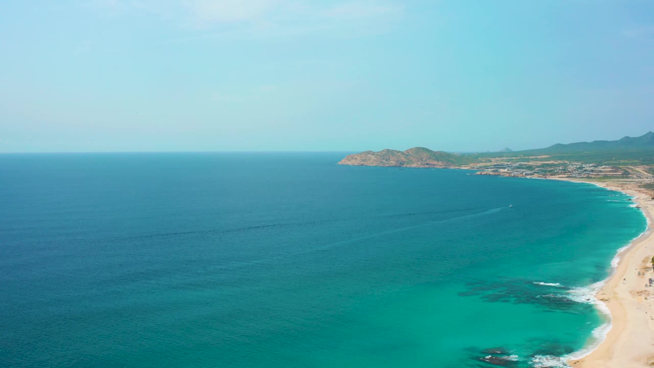 The frame holds a broad aerial composition of Desert Park Natural Reserve, with turquoise water across the center, sandy beach at right, low dry hills beyond the shore, and no visible people.