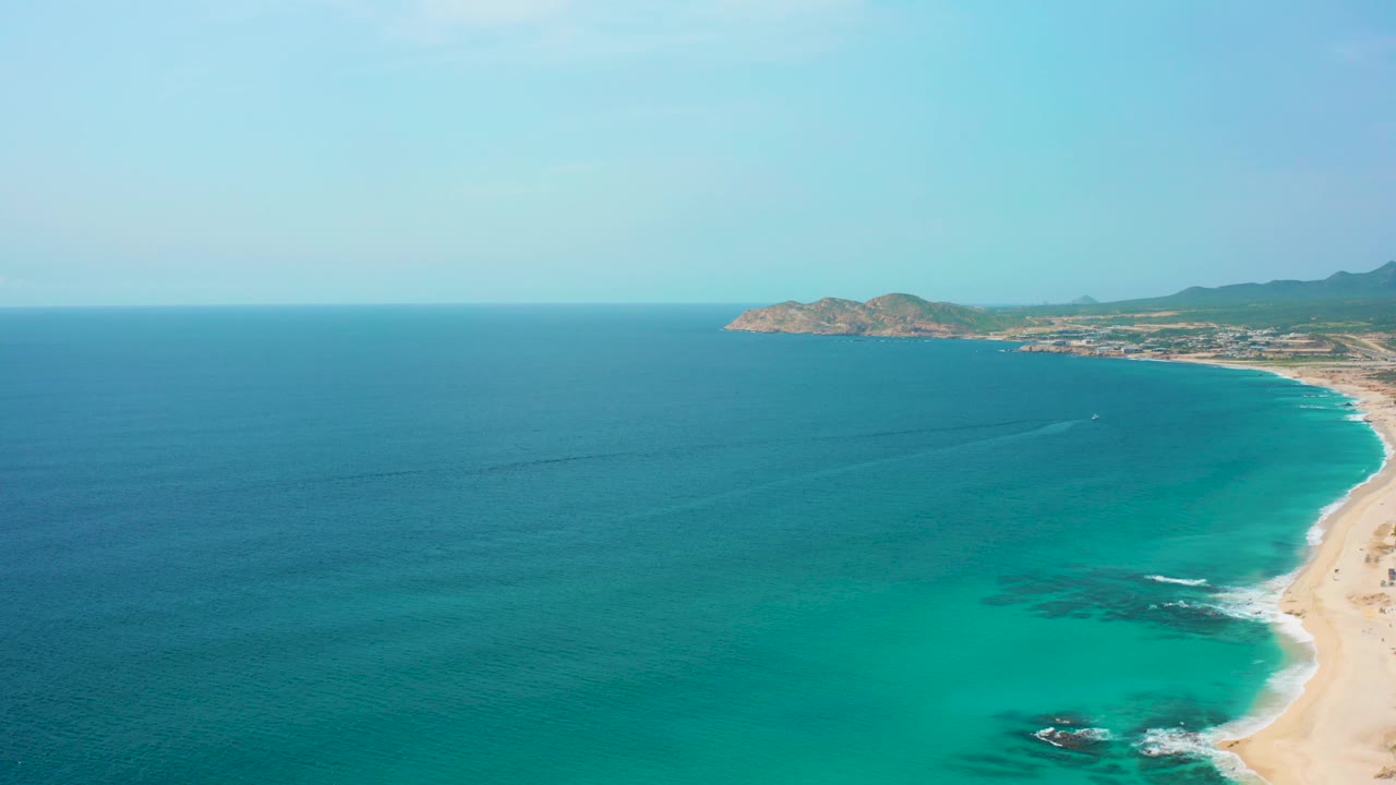 Aerial coastline with open ocean, pale beach, and dark reef patches.