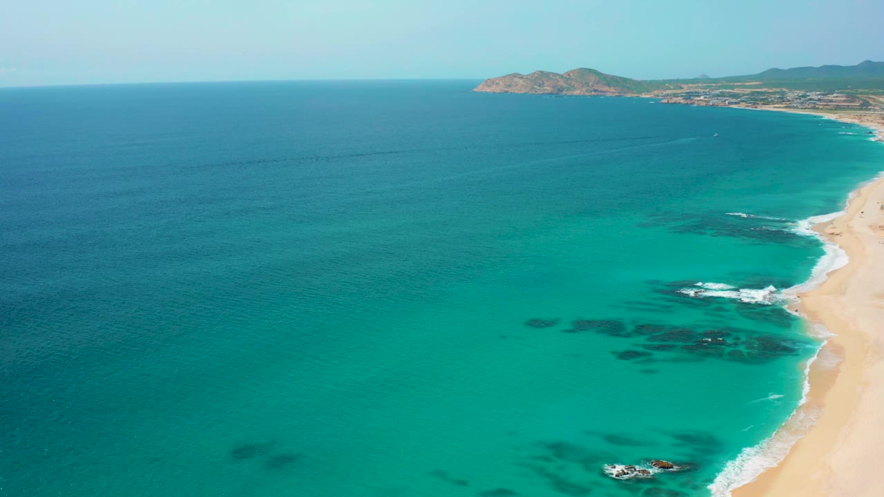 High aerial view of turquoise shallows, beach edge, and dark underwater patches.