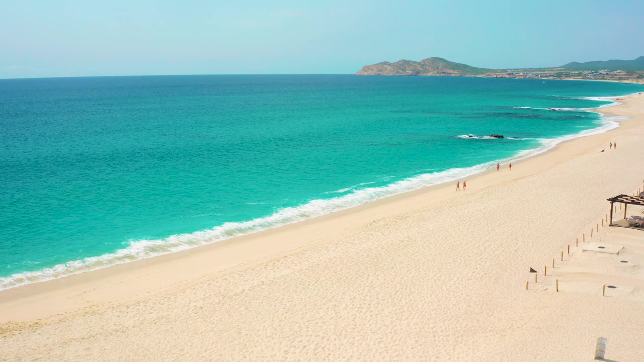 High aerial coastline with surf curling onto pale sand.