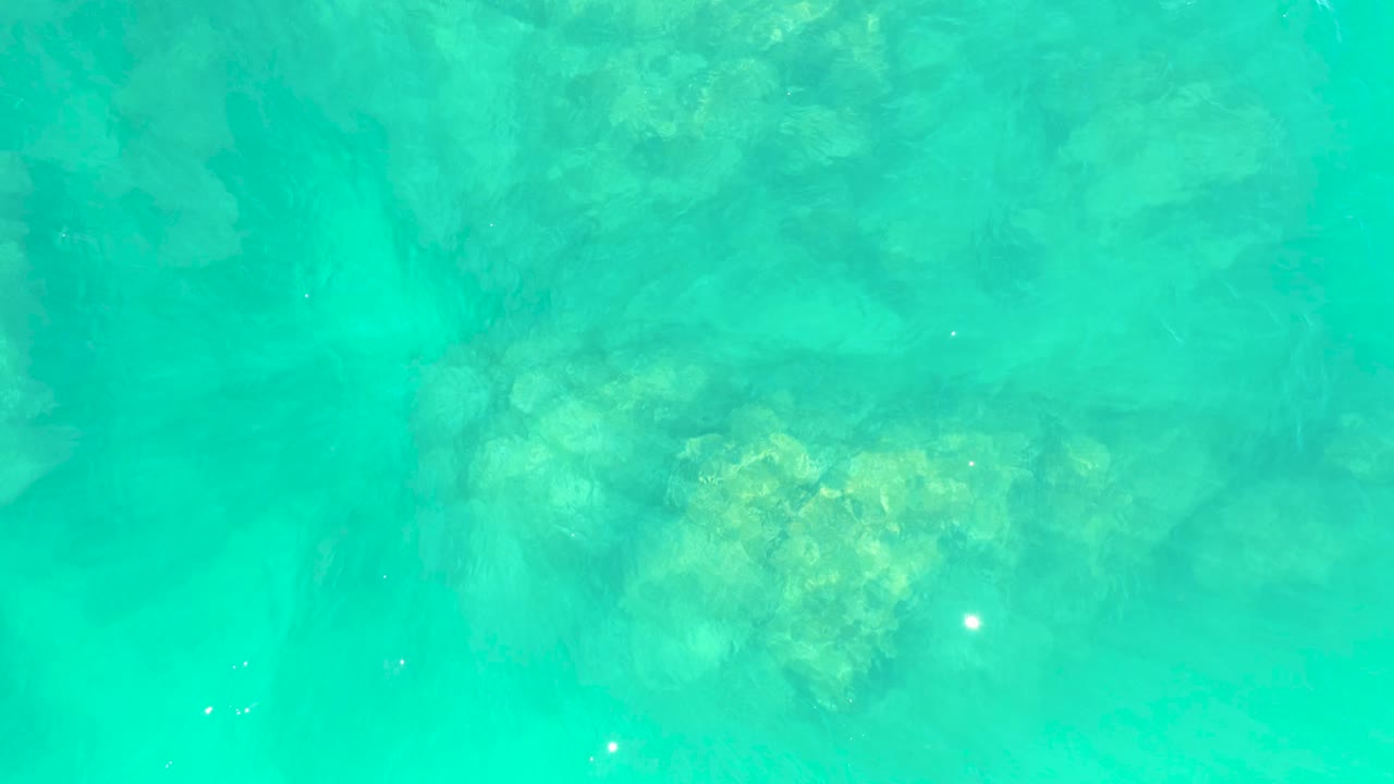 Aqua ocean water fills the frame at Marquis Los Cabos BCS Mexico, with a yellow-green submerged rock patch softened by ripples and no visible people.
