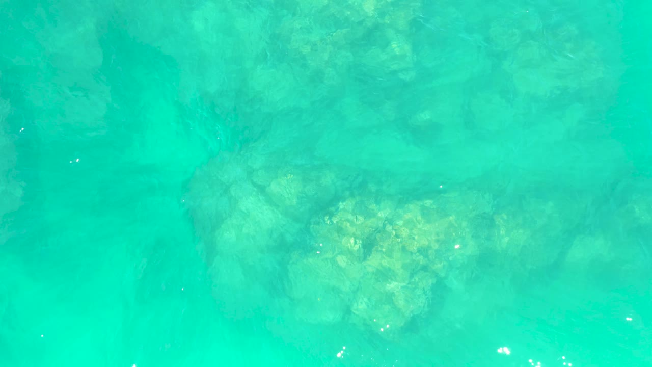 Overhead turquoise water at Marquis Los Cabos BCS Mexico shows a rock cluster below the surface with small white sun glints and no visible people.
