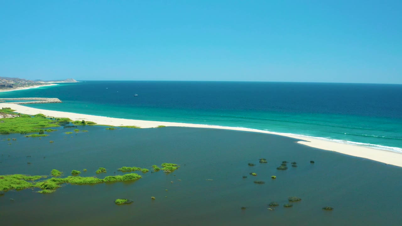 Lagoon foreground, sandbar-like beach edge, turquoise ocean, and distant coastline under blue sky.