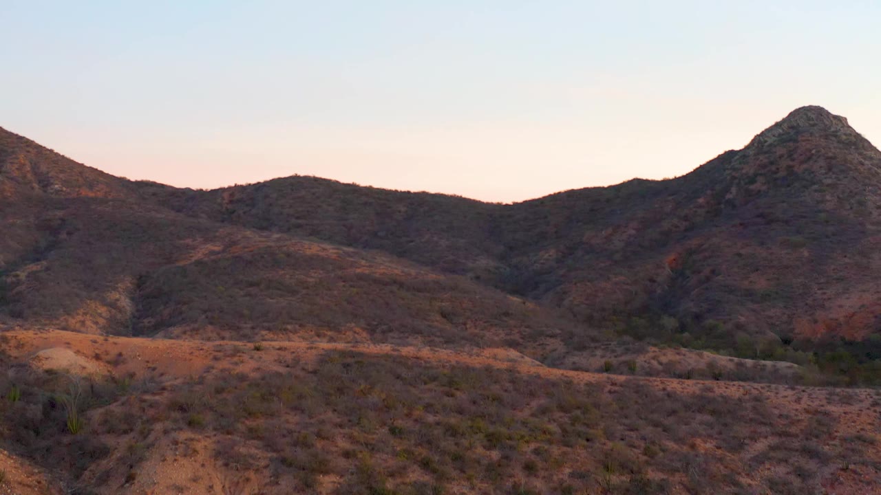 Cabo Pulmo BCS Mexico frame with sparse desert brush across the foreground, a rounded ridge leading to a pointed peak, muted evening light, and no visible people.