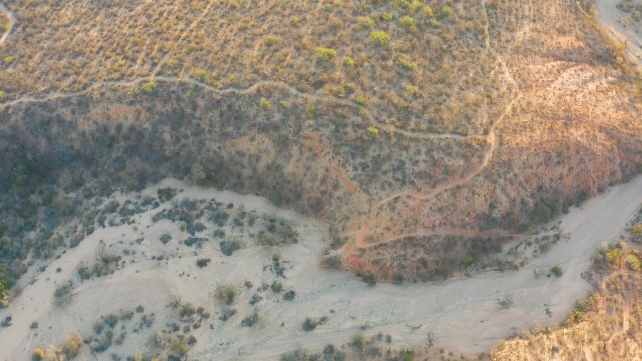 The frame looks down on a winding sandy channel in Cabo Pulmo, Mexico with faint dirt paths crossing the dry hillside and no visible people.