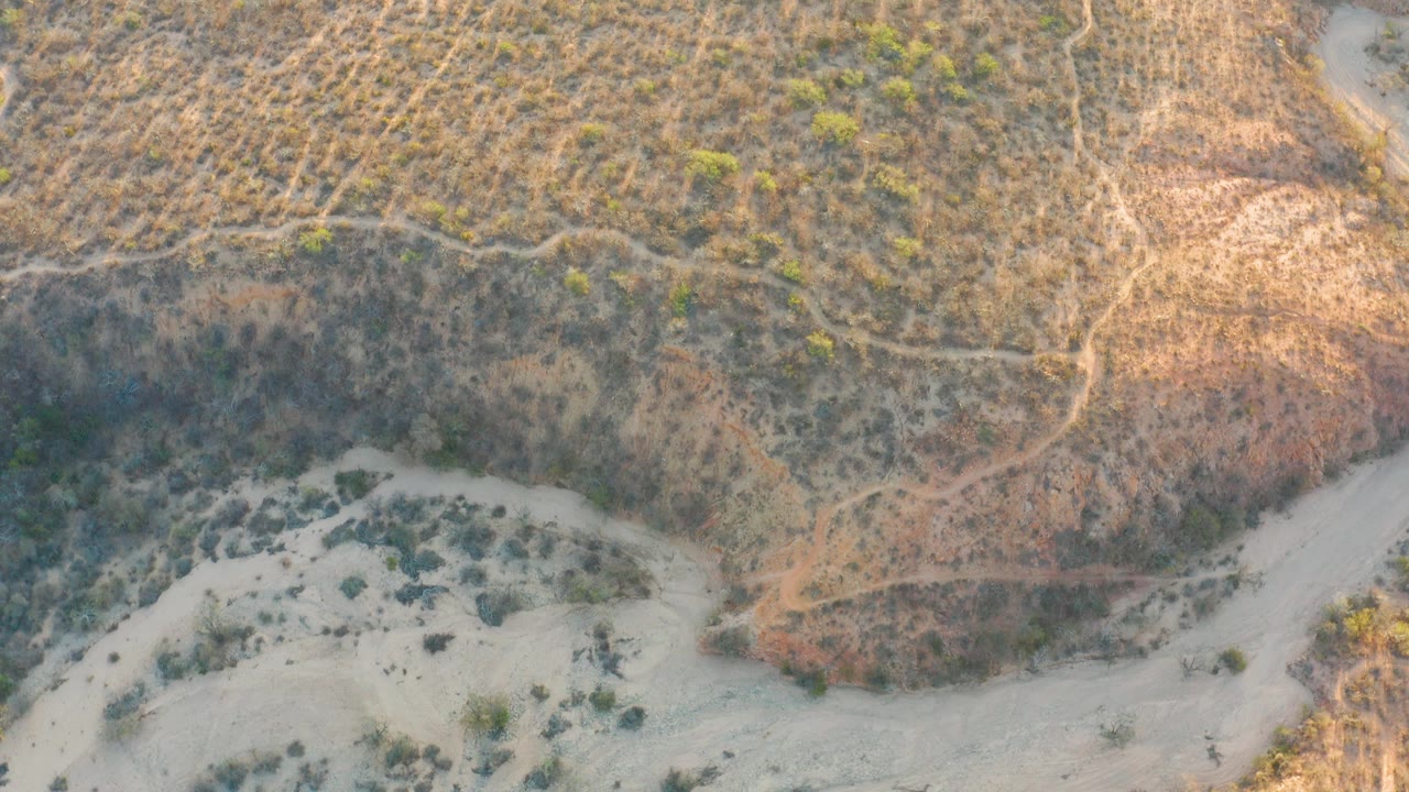 Sunlit arid slope above a pale dry riverbed