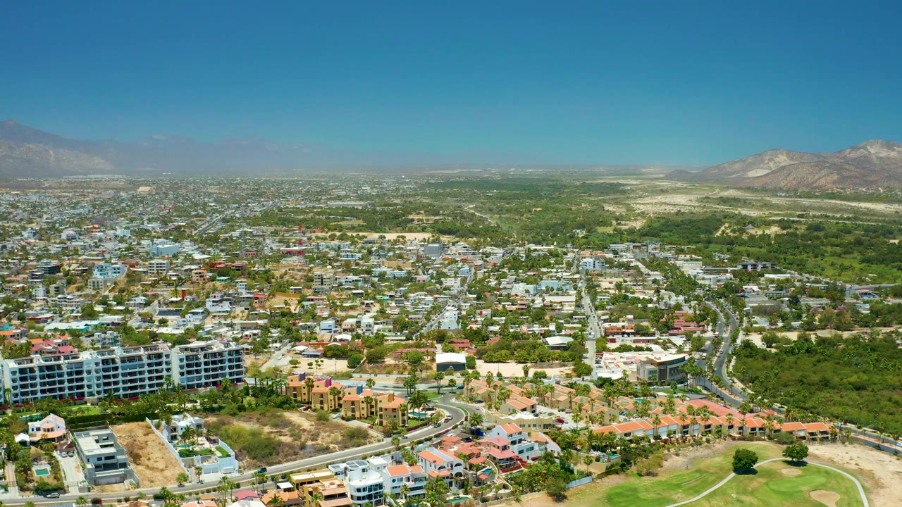 Aerial city panorama with rooftops, traffic roads, green land, and hazy mountains.