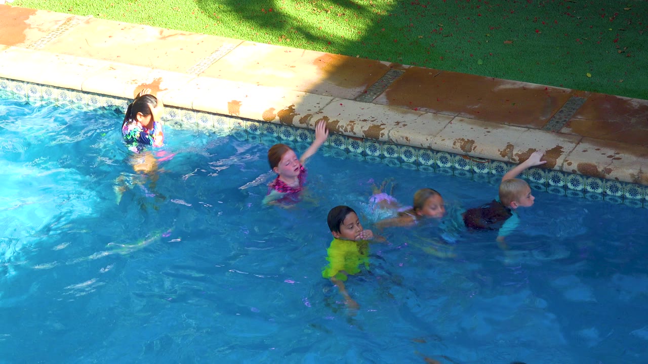 Children move through blue pool water near the tiled edge.