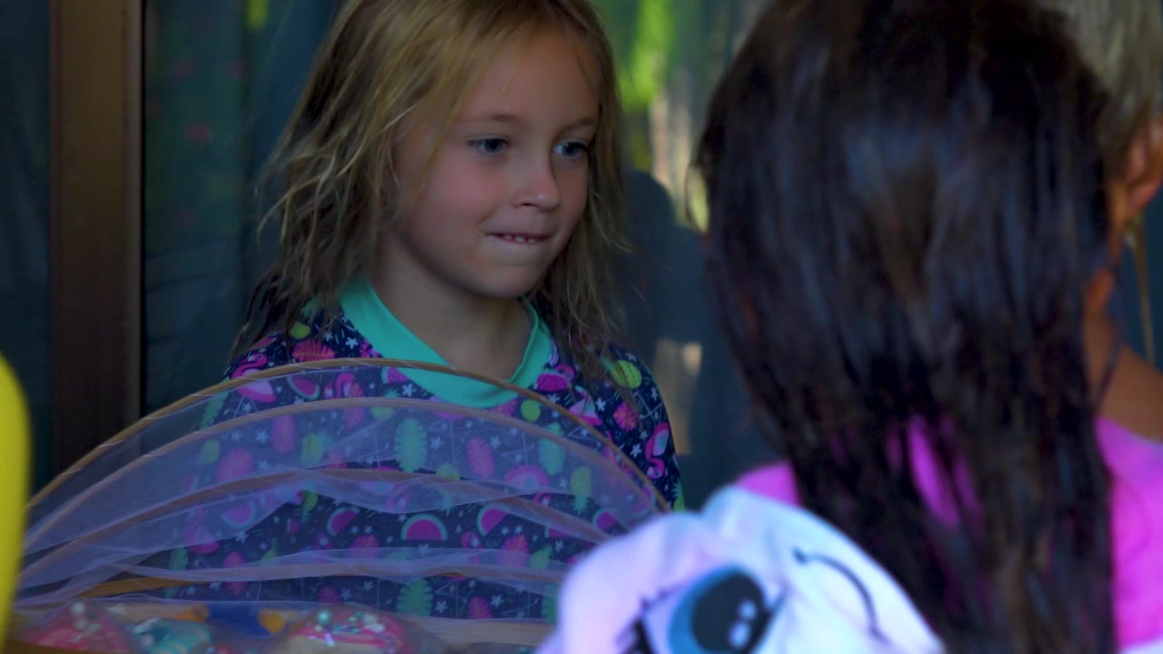 Girl looks toward children gathered by the covered table.