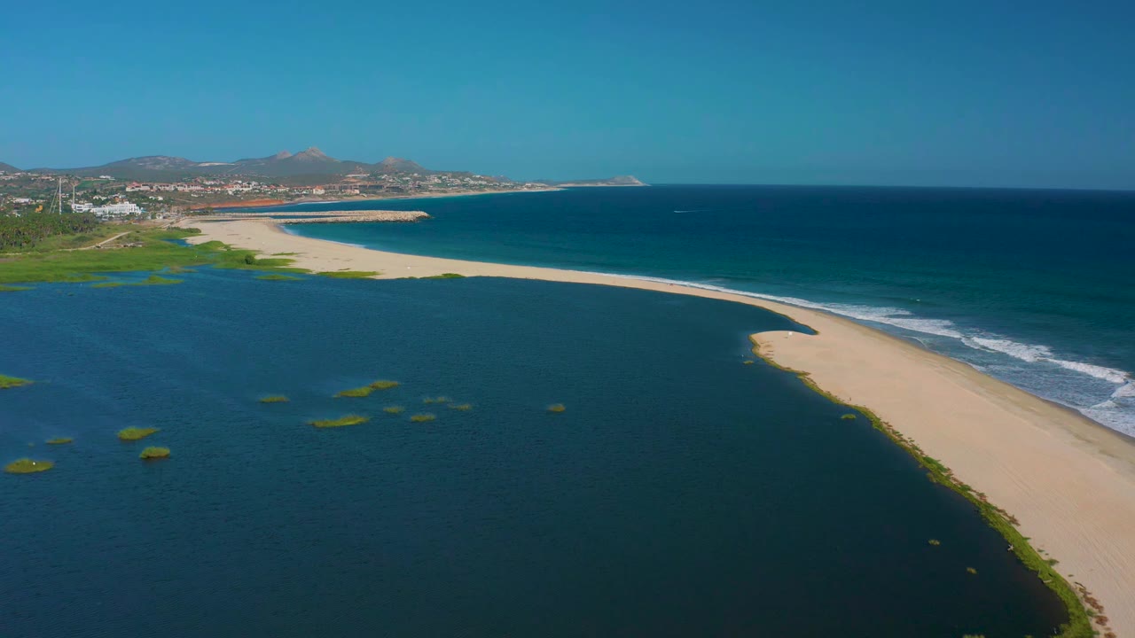 San Jose del Cabo BCS Mexico aerial view with lagoon water filling the foreground, a long sandy beach through the center, ocean beyond it, and no visible people.