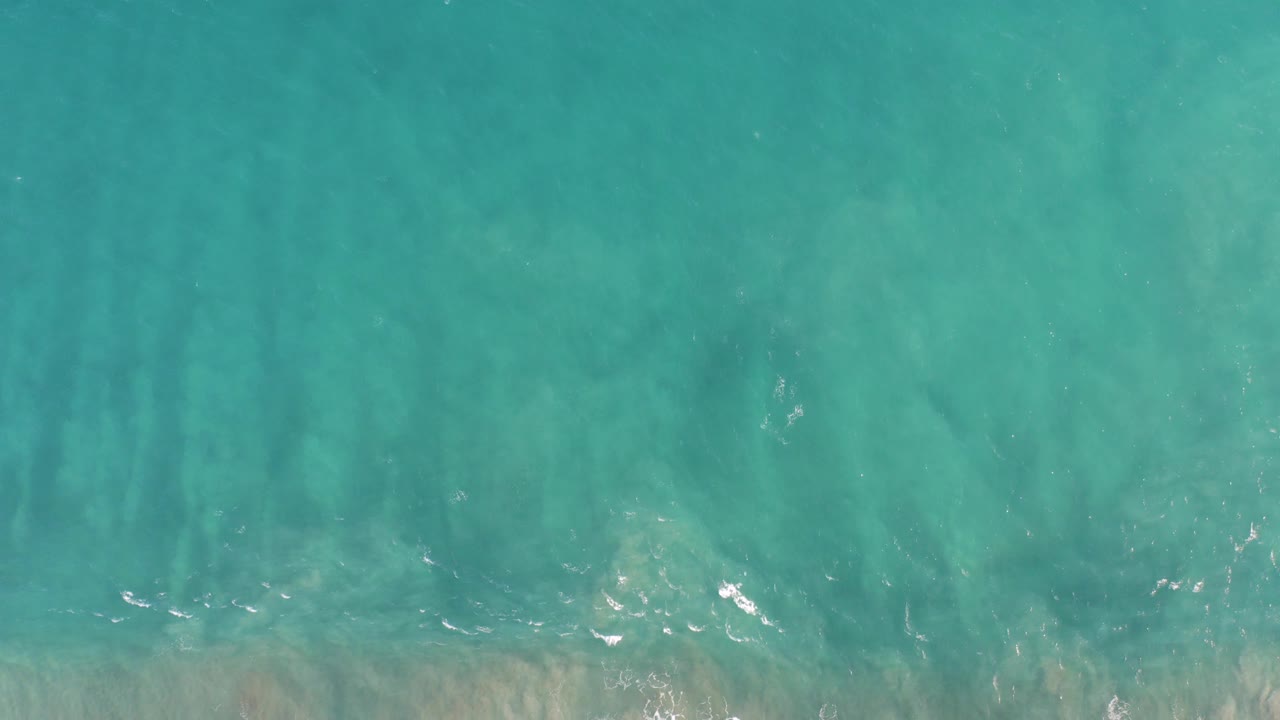 Straight-down view of turquoise shallow ocean water in San Jose del Cabo BCS Mexico, with faint sand bands and no visible people.