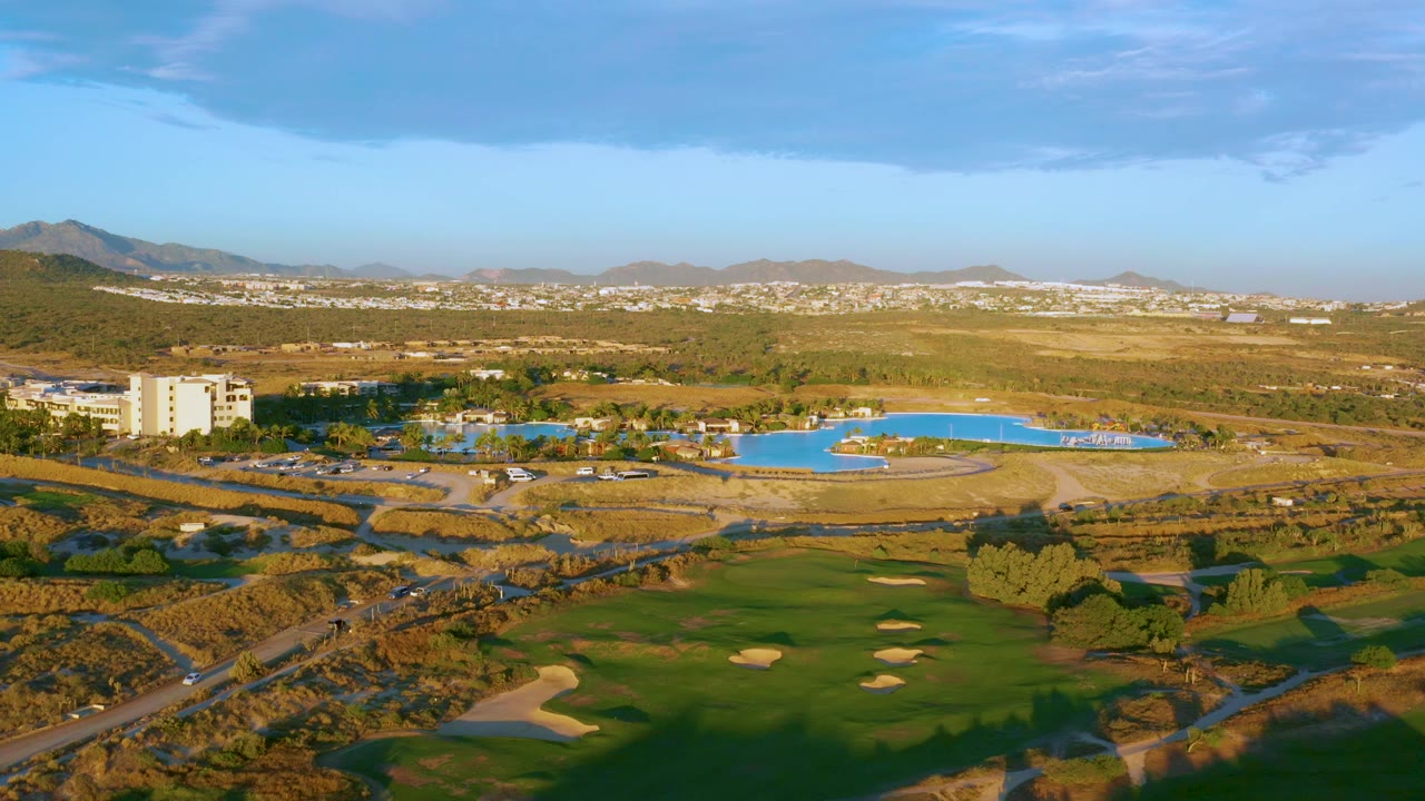 Aerial landscape with green course, blue pool, pale building, and dry hills.
