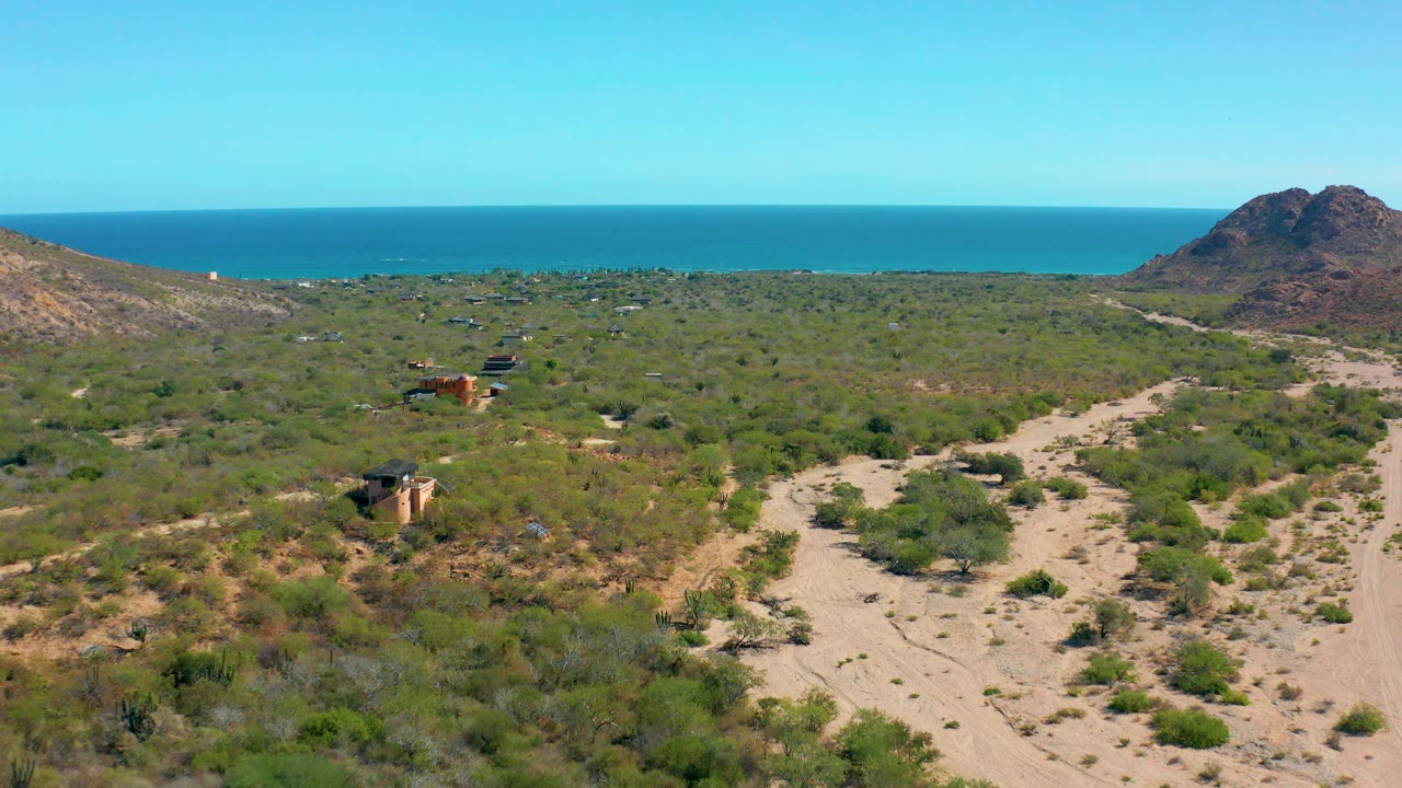 Aerial coastal desert scene with sandy wash, scattered buildings, hill, and sea.