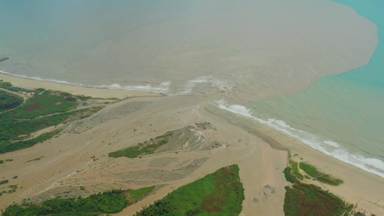 Aerial frame in San Jose Del Cabo BCS Mexico showing a sandy estuary mouth, pale muddy water, turquoise ocean edge, green vegetation, and no visible people.