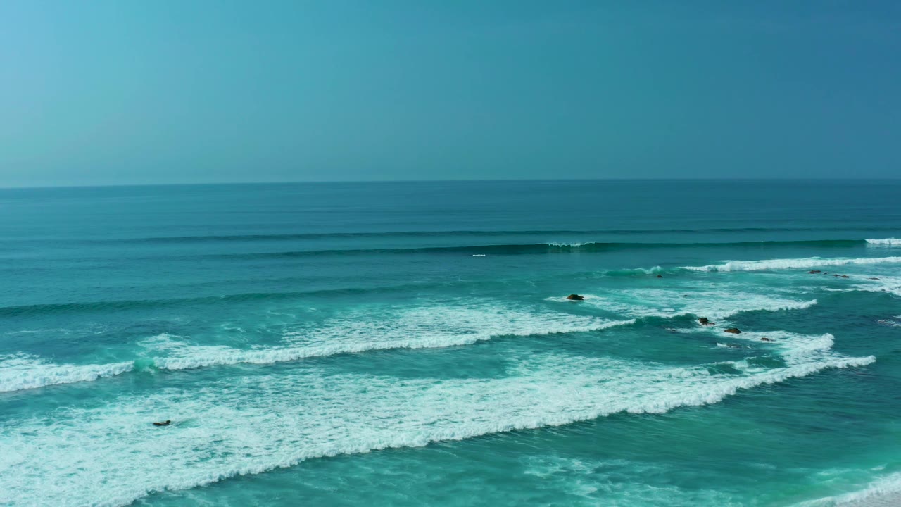 Aerial surf view with turquoise water, breaking waves, and a clear horizon.