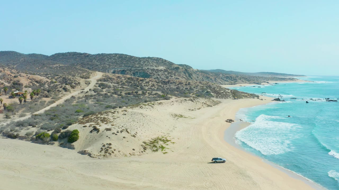 Vehicle driving along open sand with waves breaking near the shoreline.