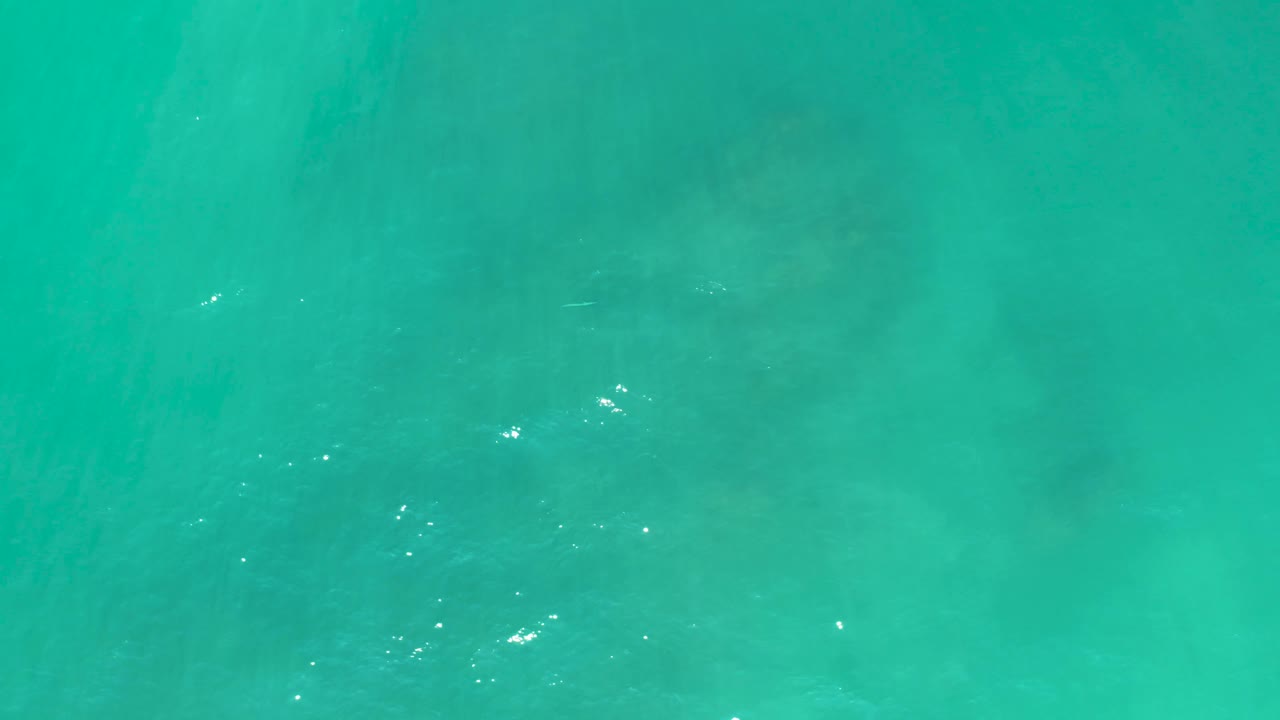 Straight-down aerial frame of turquoise ocean at San Luis Beach East Cape Los Cabos in Mexico, showing scattered sun glints over muted seabed shapes and no visible people.