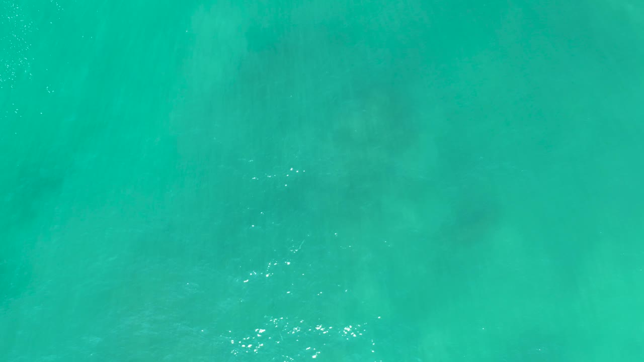 Overhead view of clear turquoise water at San Luis Beach, East Cape Los Cabos, Mexico, with faint submerged seabed shapes and no visible people.