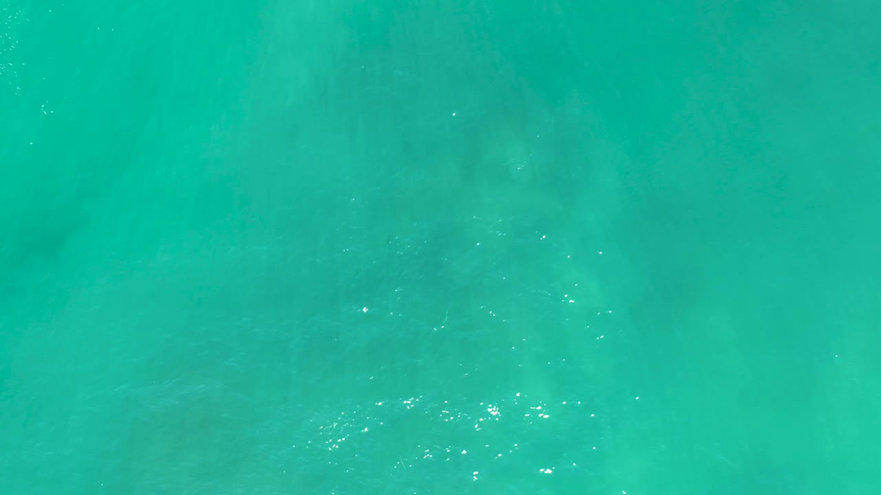 Straight-down view of turquoise water at San Luis Beach, East Cape Los Cabos, Mexico, with darker seabed texture visible through the shallows and no visible people.