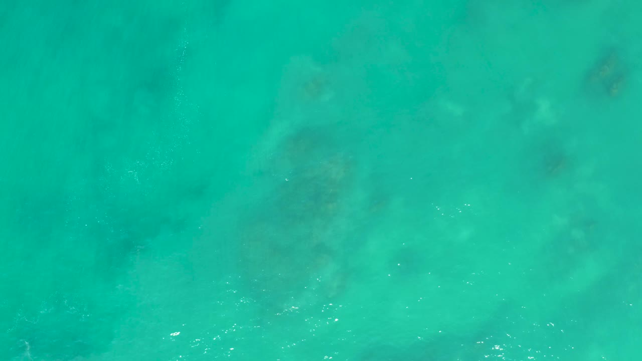 Top-down turquoise ocean water with darker underwater patches and small white bubbles.