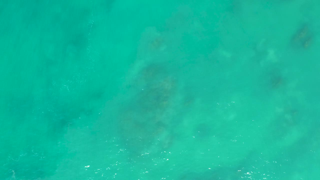 Clear turquoise sea at San Luis Beach in Mexico, showing faint submerged formations beneath the surface and scattered bubbles, no visible people.