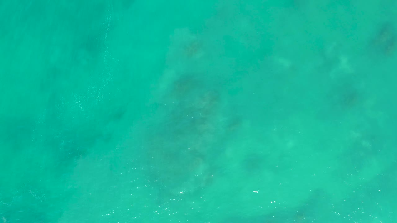 Turquoise sea surface at San Luis Beach in Mexico, with cloudy underwater texture and small white bubble clusters crossing the frame, no visible people.