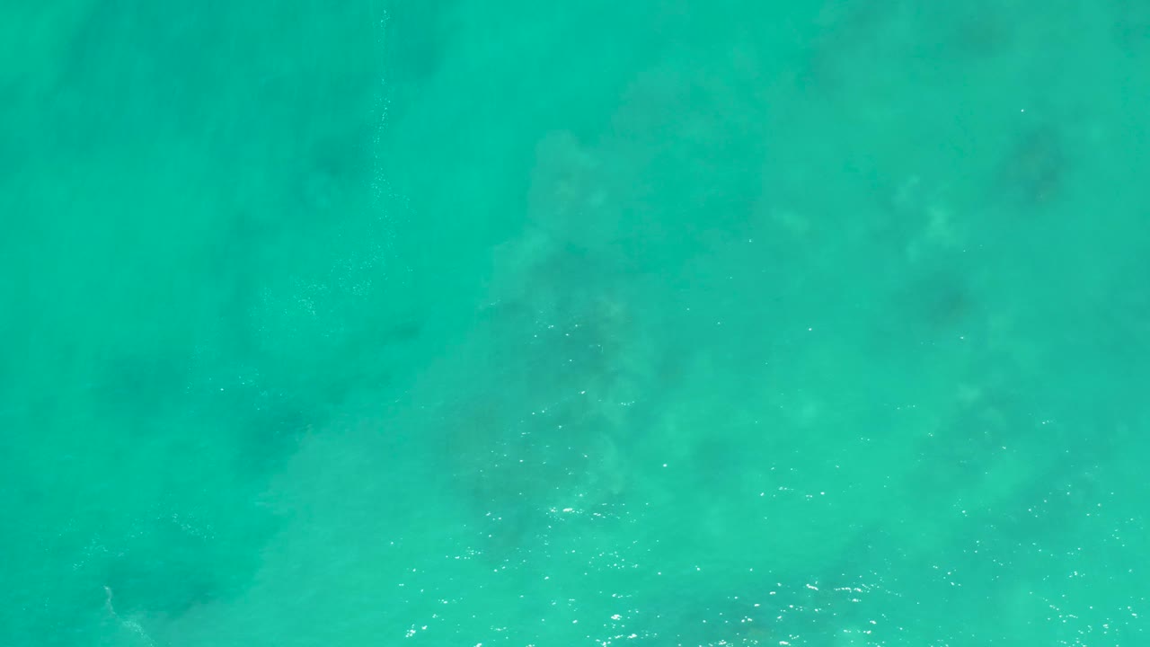 Turquoise water with diffuse foam and darker seabed patches underneath.