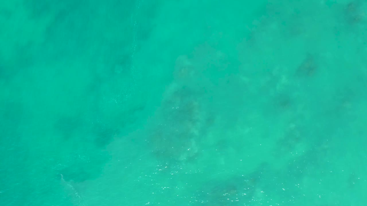 Clear blue-green ocean water over pale seabed texture at San Luis Beach East Cape Los Cabos, with small ripples and no visible people.