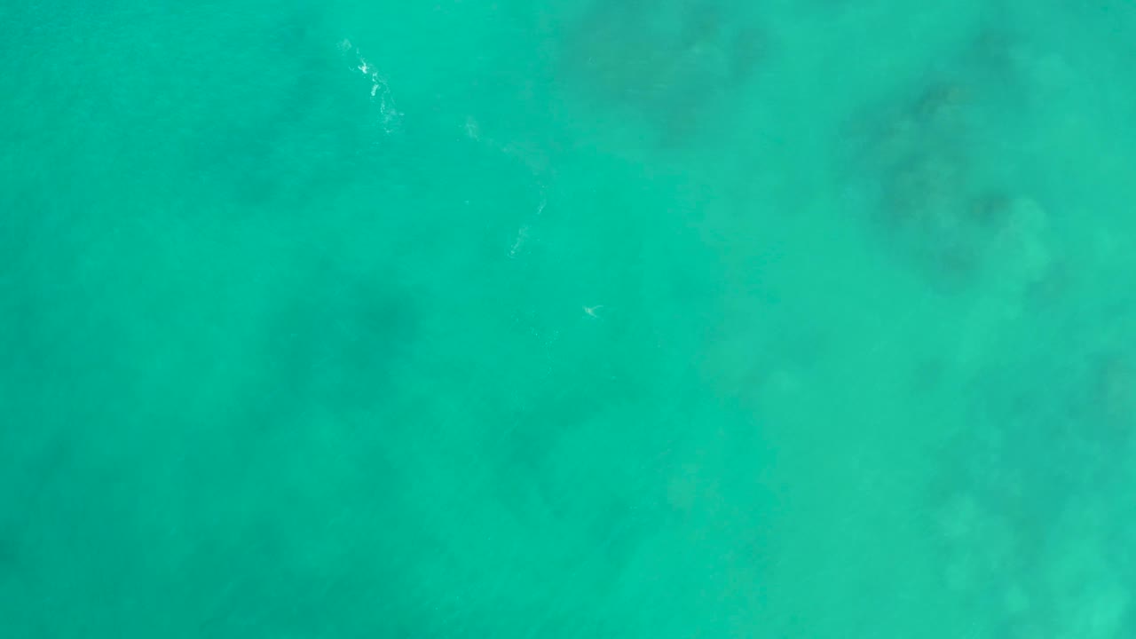 Aerial-looking view of San Luis Beach turquoise water with muted seabed and coral shapes softened by the surface, with no visible people.