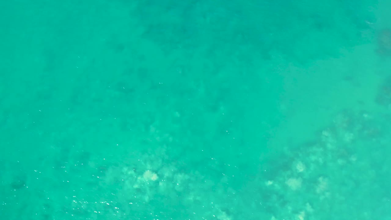 Overhead frame of clear turquoise water with faint lighter and darker underwater patches at San Luis Beach, East Cape Los Cabos, Mexico, and no visible people.