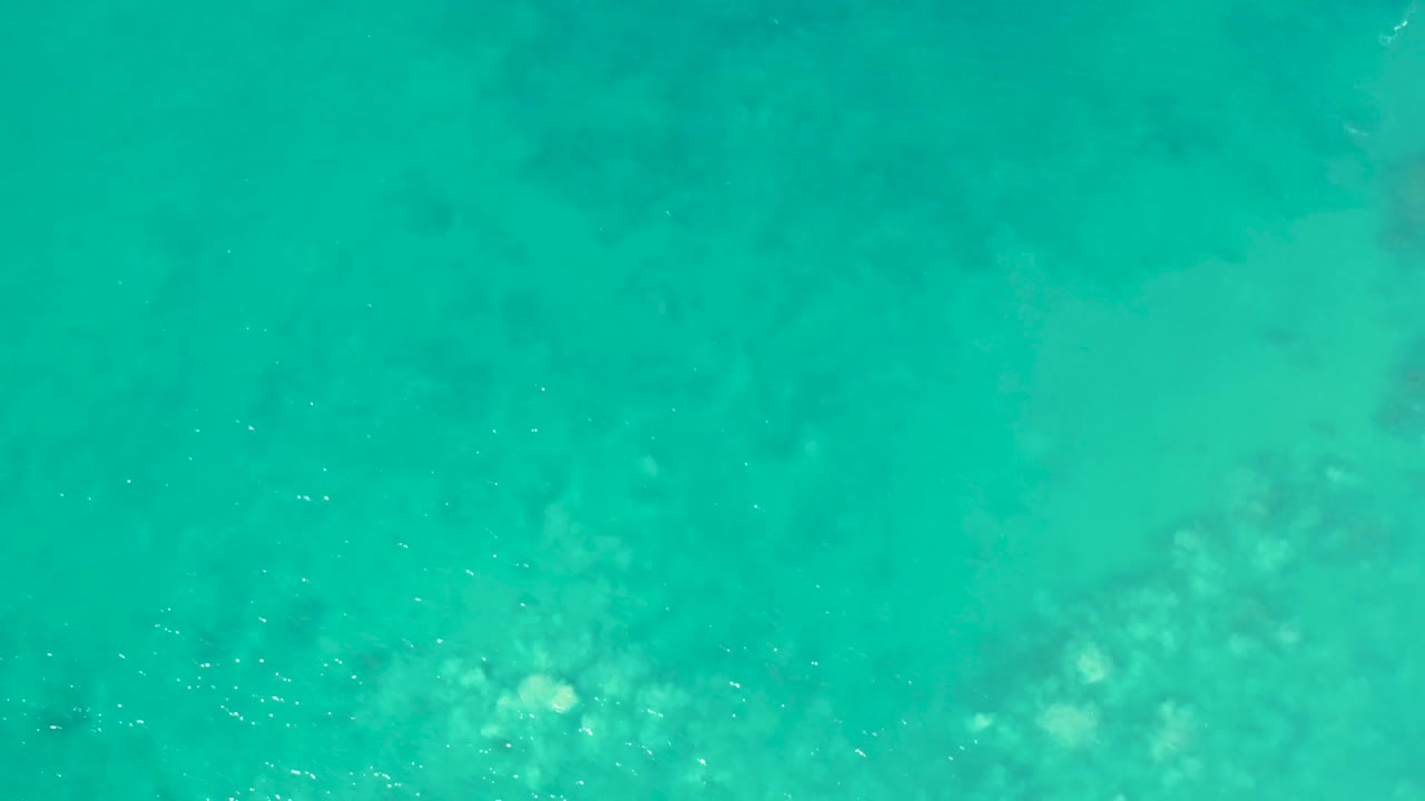 Top-down ocean frame with turquoise water, pale reef-like seabed areas, and small bright surface disturbances in Mexico, with no visible people.