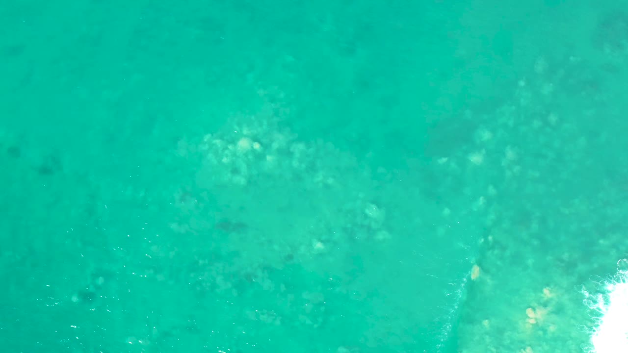 Clear turquoise water with mottled underwater rock patches and a white wave breaking from the right.